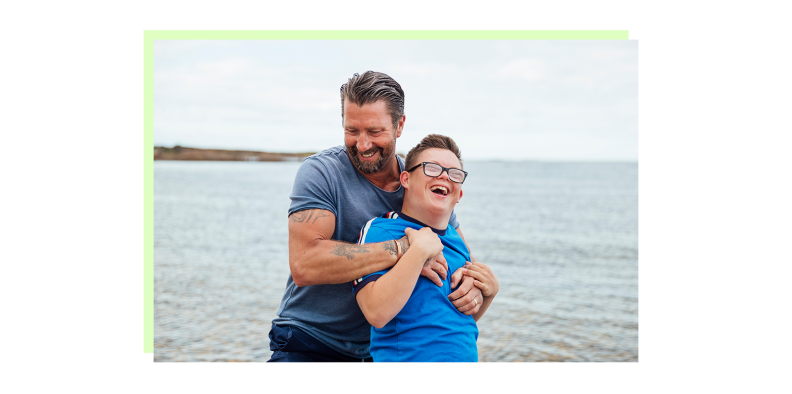 An adult hugging a child with special needs at the beach.