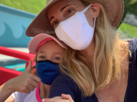 A young girl and a her mom both wearing masks and hats on a Disneyland ride