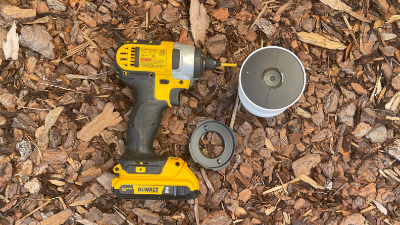 A drill, mounting base with screws, and the new Nest Cam sit on a pile of mulch.