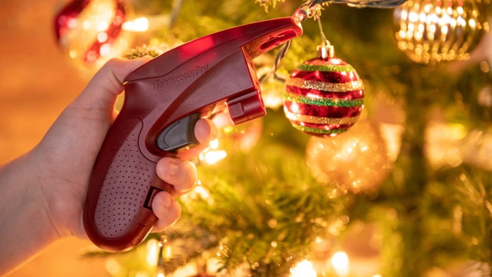Red glue-gun-shaped tool next to a lit Christmas tree with sparkling holiday string lights on it and ornaments
