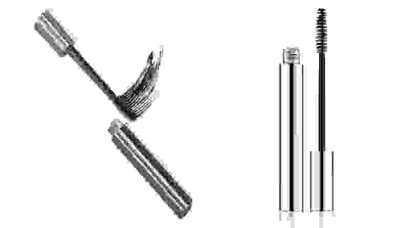 On the left: The silver tube of the Clinique Naturally Glossy Mascara lays on a white background with the wand outside of the cylindrical tube swatching the mascara. On the right: The same tube of mascara stands up with the wand standing next to the tube.