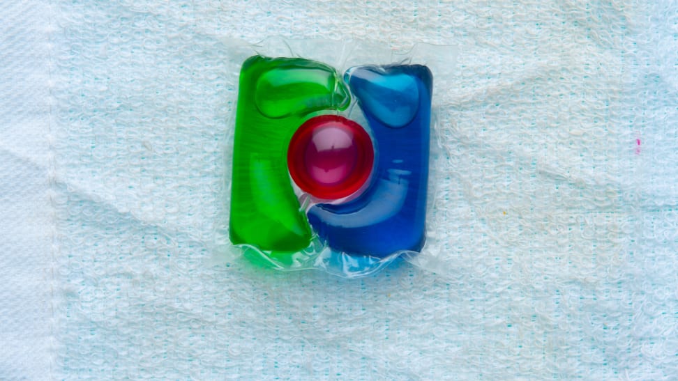 A green, blue, and red dishwasher detergent pod sits on a blue towel