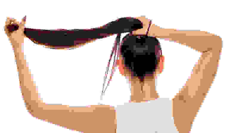 A photo of a woman tying her hair into a ponytail.