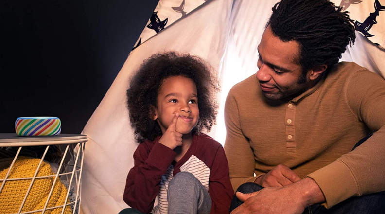 A family sits on the floor with an Amazon Echo Dot (third-generation) Kids Edition speaker nearby