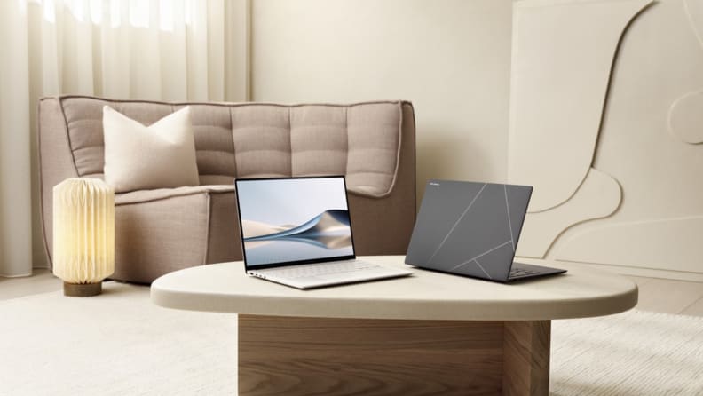 Two Asus Zenbook S 14 laptops on the coffee table of a neutral-colored minimalist living room with sofa and paper lantern.