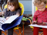 Two children read picture books outside.