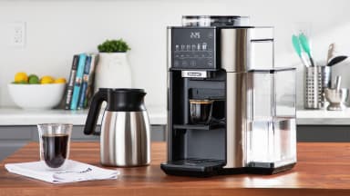 The De'Longhi True Brew on a countertop with a pot of coffee and cup of coffee next to it.