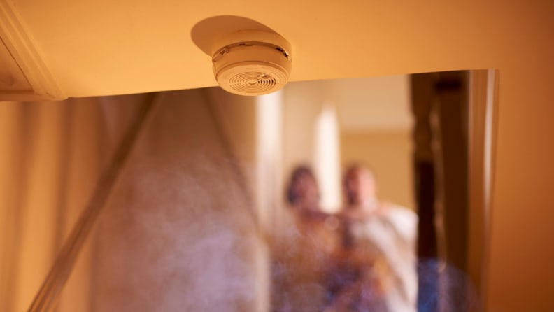 Smoke detector detecting smoke in a room with people in the house in the background.
