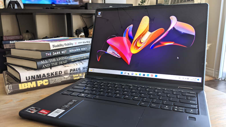 An open and powered on laptop sitting on a coffee table with a short stack of books to its side