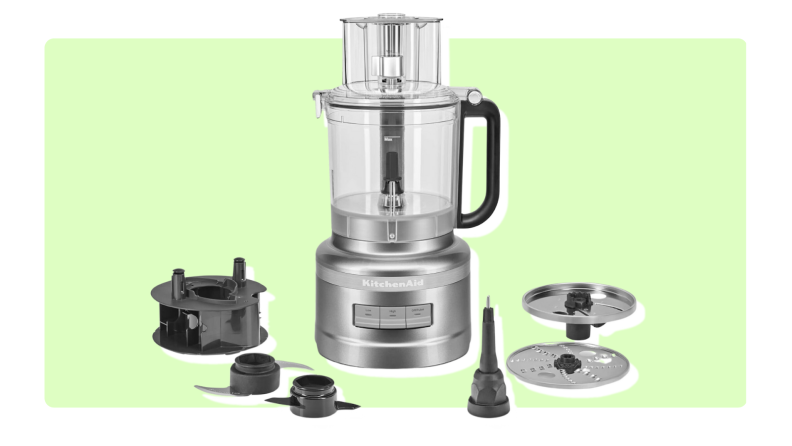 The KitchenAid 13-Cup Food Processor surrounded by multiple attachments in front of green background.