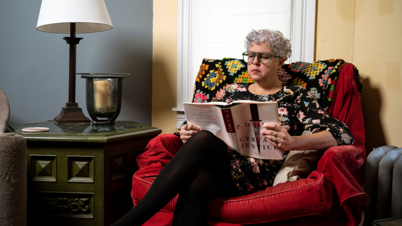 Woman sitting in red chair in living room reading a book while wearing green reading glasses.