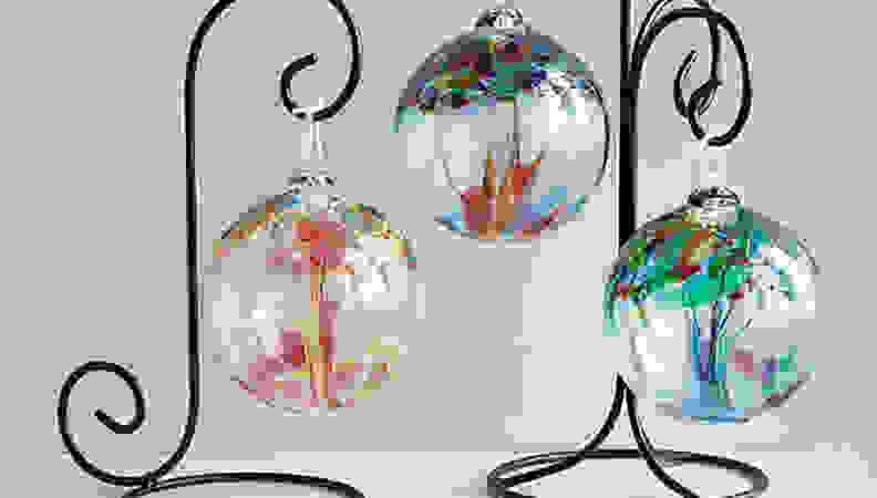 assorted colored glass globes hanging from ironlike stand on grey background.