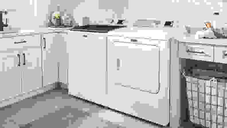 A white washer and dryer next to a laundry basket and white cabinets.