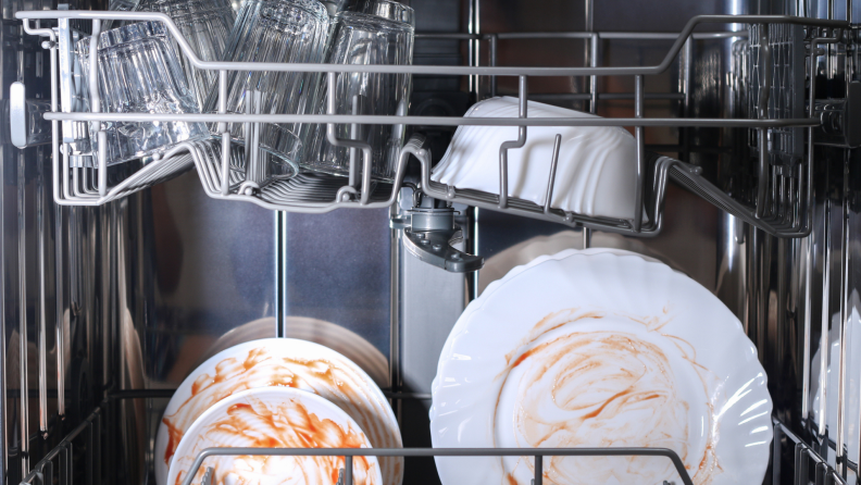 White plates in dishwasher with red sauce stains on them.