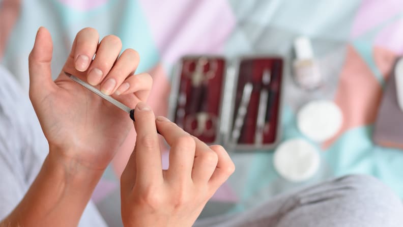 A person holding their left hand palm up and using their right hand to file the fingernails on the left hand. Nail tools are in the background.