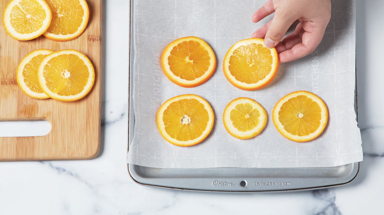 Orange slices being laid out on a baking sheet with parchment.