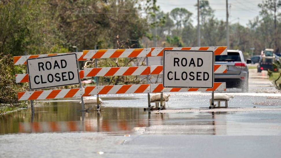 Orange and white signs block a road that is flooded with Road Closed signs