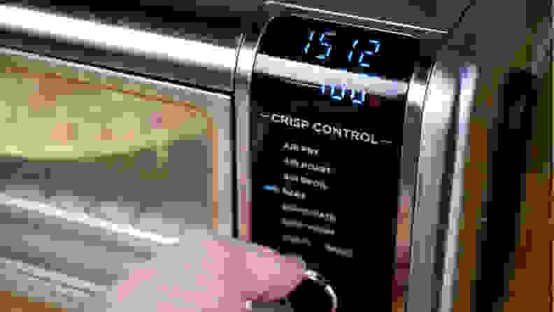 A person turns the dial on the Ninja Foodi oven while setting the temperature and time.