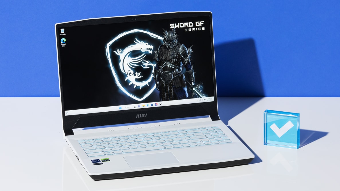 The MSI Sword 15 opened on a white surface with a blue Reviewed checkmark paperweight next to it.