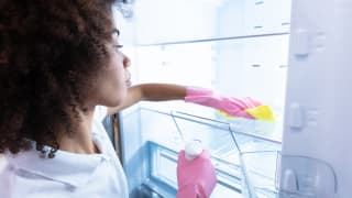 A person wearing rubber gloves wipes down the shelves in a fridge with a cloth