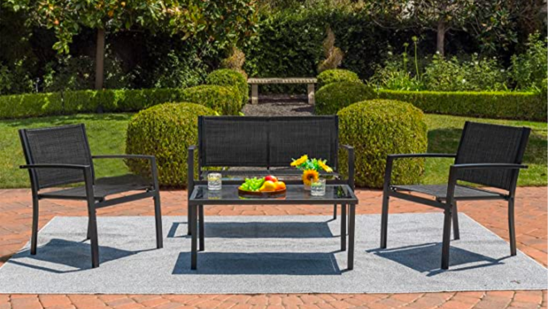 An image of a black and black mesh chair, bench and table set on a brick patio.