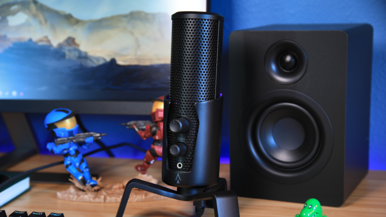 The Monoprice Dark Matter Sentry streaming microphone next to a speaker and action figures, sitting on a desktop.