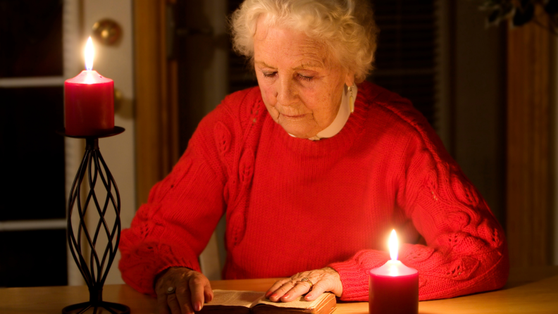 Older woman reading next to lit candles in a dark room