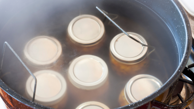 Seven glass jars are sitting in a pot of water being cooked.