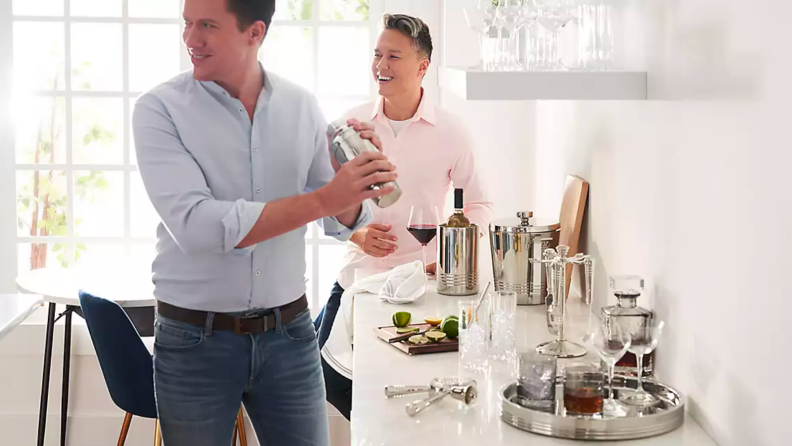 An image of two men standing in an entertaining space, one of whom is holding and using a cocktail shaker.