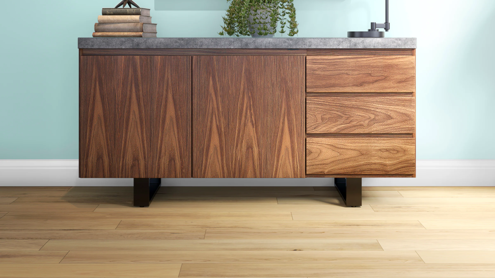 A stained wooden cabinet with several drawers rests on vinyl plank flooring against a mint-green wall.