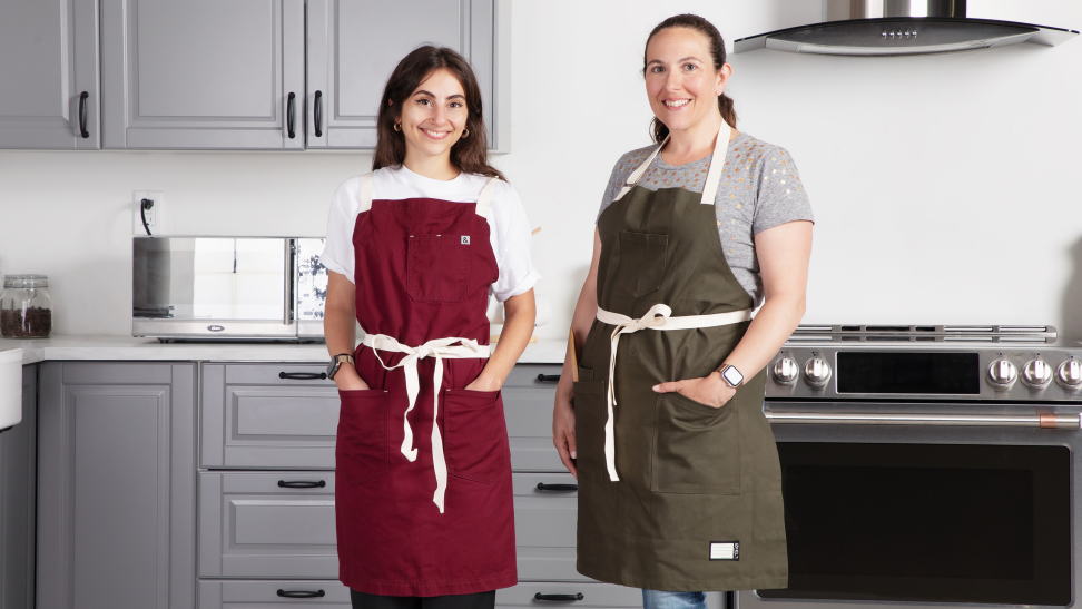 Two people wearing aprons in a kitchen set