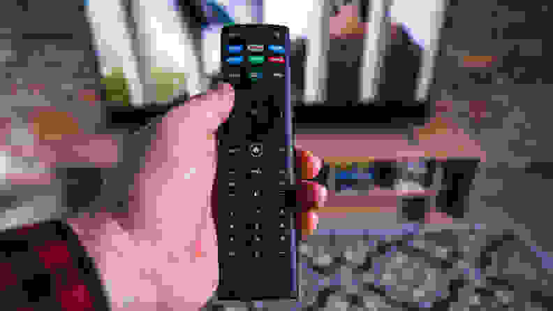 A hand holds the remote to a Vizio smart TV.