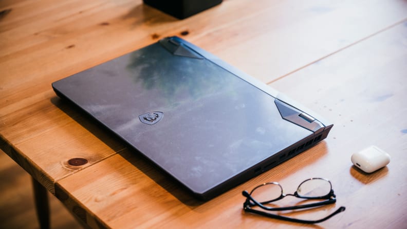 A closed laptop on top of a desk with a pair of glasses and an ear bud case next to it.