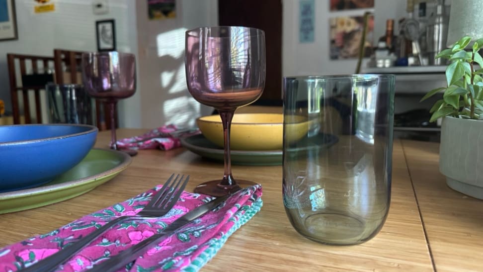 A purple wine glass and green water glass on a dining room table.