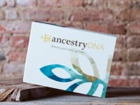 Ancestry DNA kit in a box in front of brick wall.