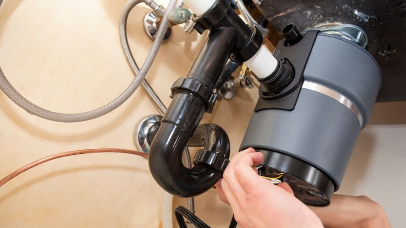 Person unplugging garbage disposal under sink.