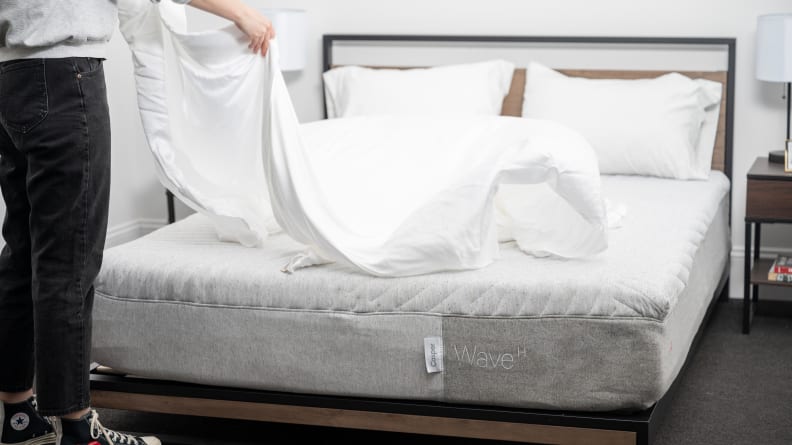 A person spreading sheets on top of a mattress