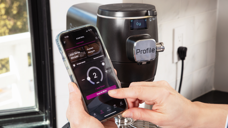 A person holds a phone showing the Smart HQ app in front of the smart mixer.