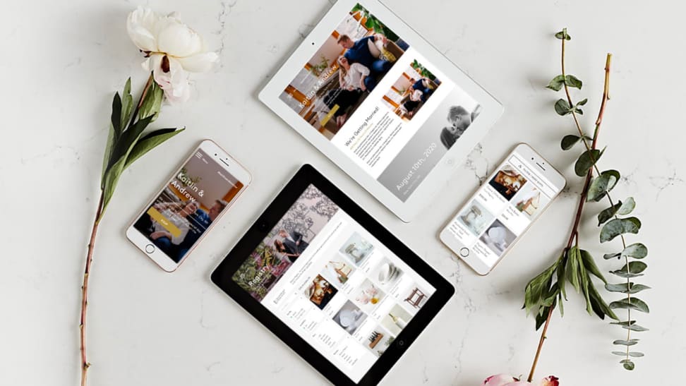 Two tablets and cell phones display wedding registries next to two flowers on a surface.