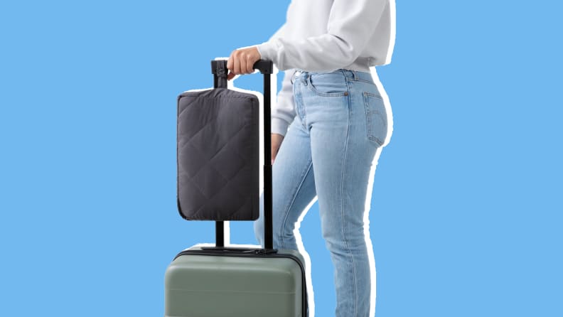 Person standing next to suitcase with the Tuft & Needle Travel Anywhere Blanket attached.
