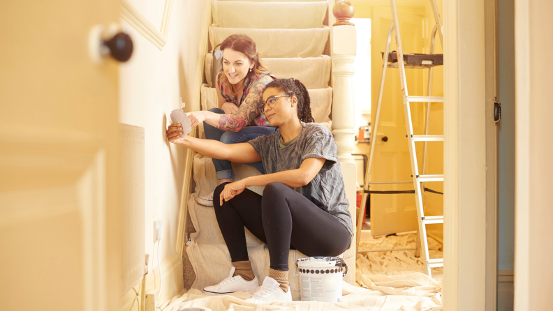 women hold paint swatches up to wall