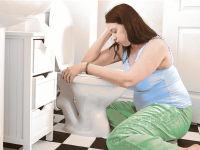 A pregnant person rests over a toilet, sick with morning sickness.