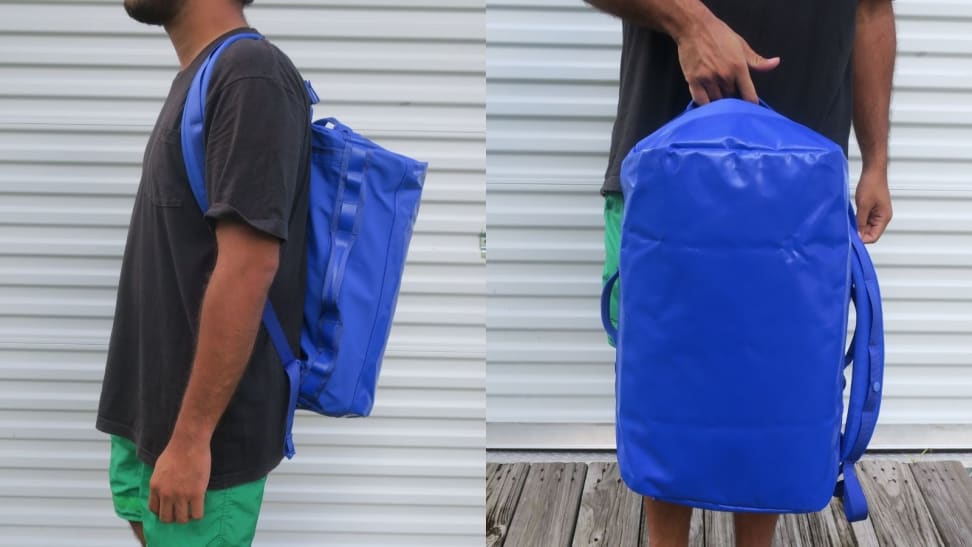 Man in black T-shirt and green shorts wearing a blue Baboon to the Moon Go-Bag on his back, man holding blue Baboon to the Moon Go-Bag by top handle.