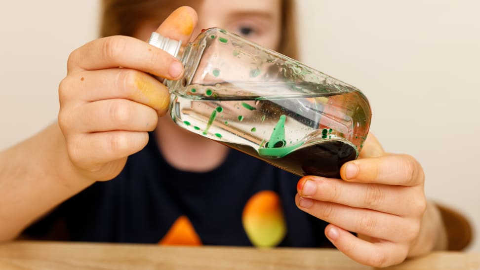 A boy plays with a sensory bottle that includes a tiny sailboat.