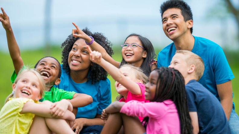 Children point to the sky to show their camp counselors something at a summer camp.