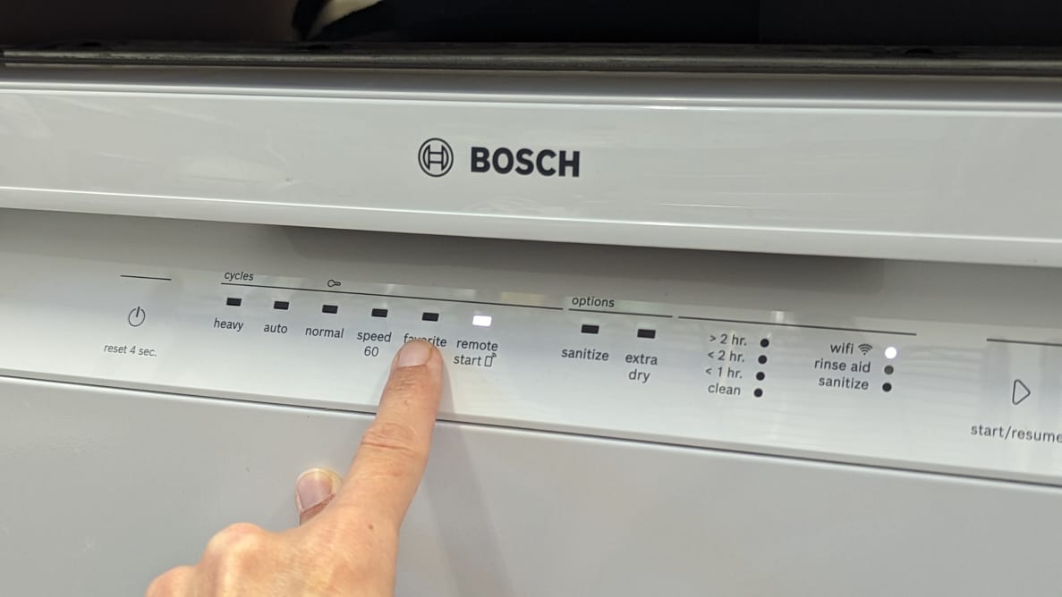 A person pointing at the Bosch 100 Series dishwasher's control buttons.