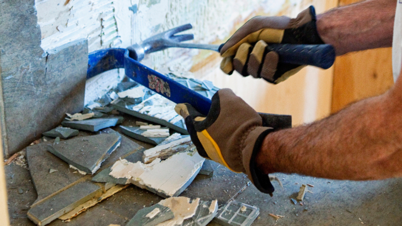 A person pries a tile off a wall.