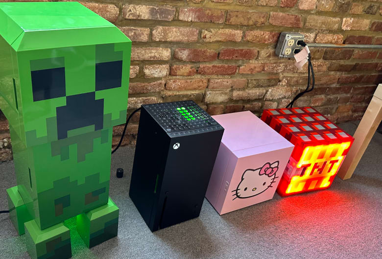 n array of novelty thermoelectric coolers set up to test in our office. They are, from left to right, a cooler in the shape of the Creeper enemy from Minecraft, an XBox, a small cube-shaped cooler with Hello Kitty's face on the front, and a cooler with the shape and design of a Minecraft TNT block.