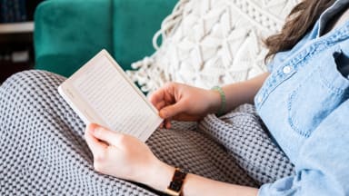 A woman sitting on the couch using an e-reader to read a book.
