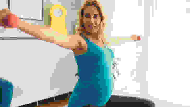 Pregnant Woman Exercising At Home with Dumbbells and with fitness ball